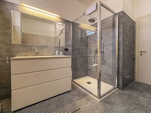 Un baño moderno con ducha envuelta en vidrio, un espejo grande y un tocador con cajones.