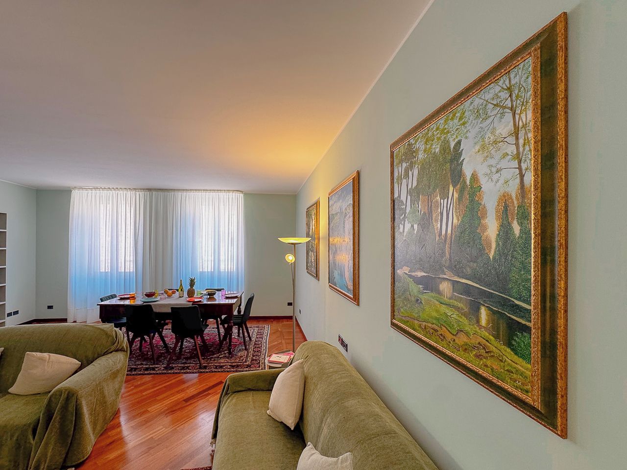 Un salon avec un canapé, un coin repas avec une table et des chaises, et un grand tableau encadré accroché au mur.