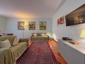 Una sala de estar con un sofá, un tapete estampado, un televisor y obras de arte en la pared.