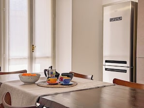 Un comedor con una mesa preparada para dos personas, un cuenco de fruta y una cafetera.