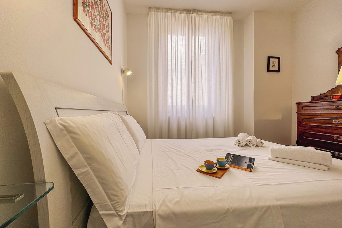 Habitación de hotel con cama, mesita de noche, lámpara, ventana con cortinas y cómoda de madera.
