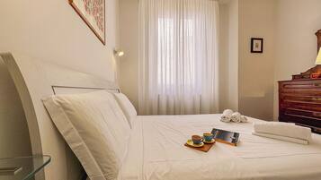 Habitación de hotel con cama, mesita de noche, lámpara, ventana con cortinas y cómoda de madera.