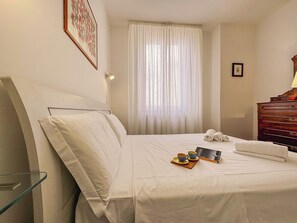 Habitación de hotel con cama, mesita de noche, lámpara, ventana con cortinas y cómoda de madera.