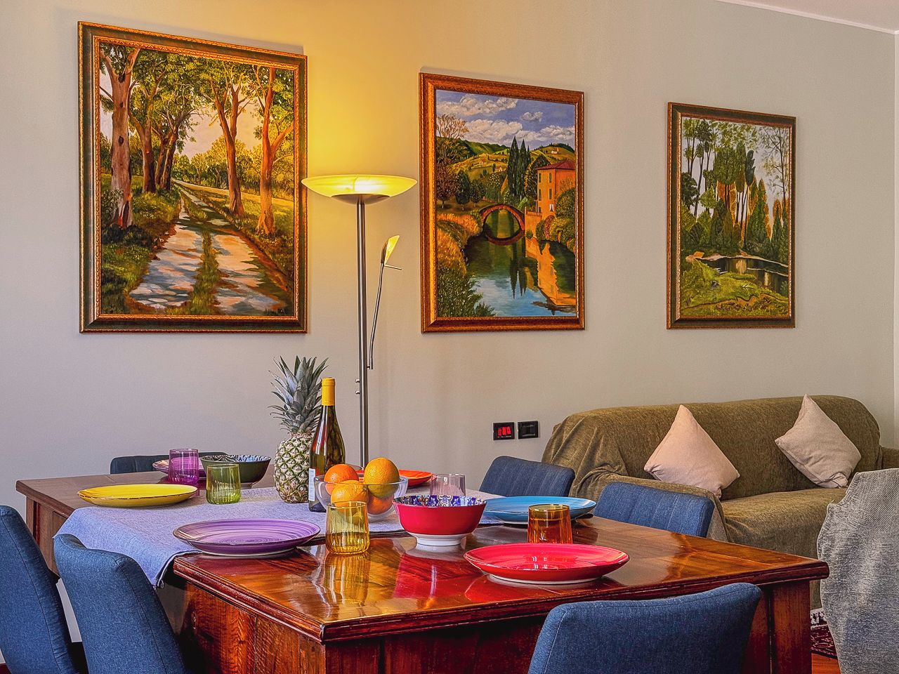 A dining area with a wooden table set for four, surrounded by blue chairs. There are paintings on the wall above the table.