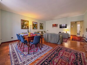 Ein Essbereich mit Tisch, Stühlen und einem Fernseher. Teppiche liegen auf dem Boden und Gemälde hängen an den Wänden.