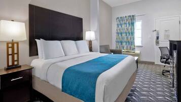 A hotel room with a large bed, two bedside lamps, a desk with a chair, and a window with curtains.