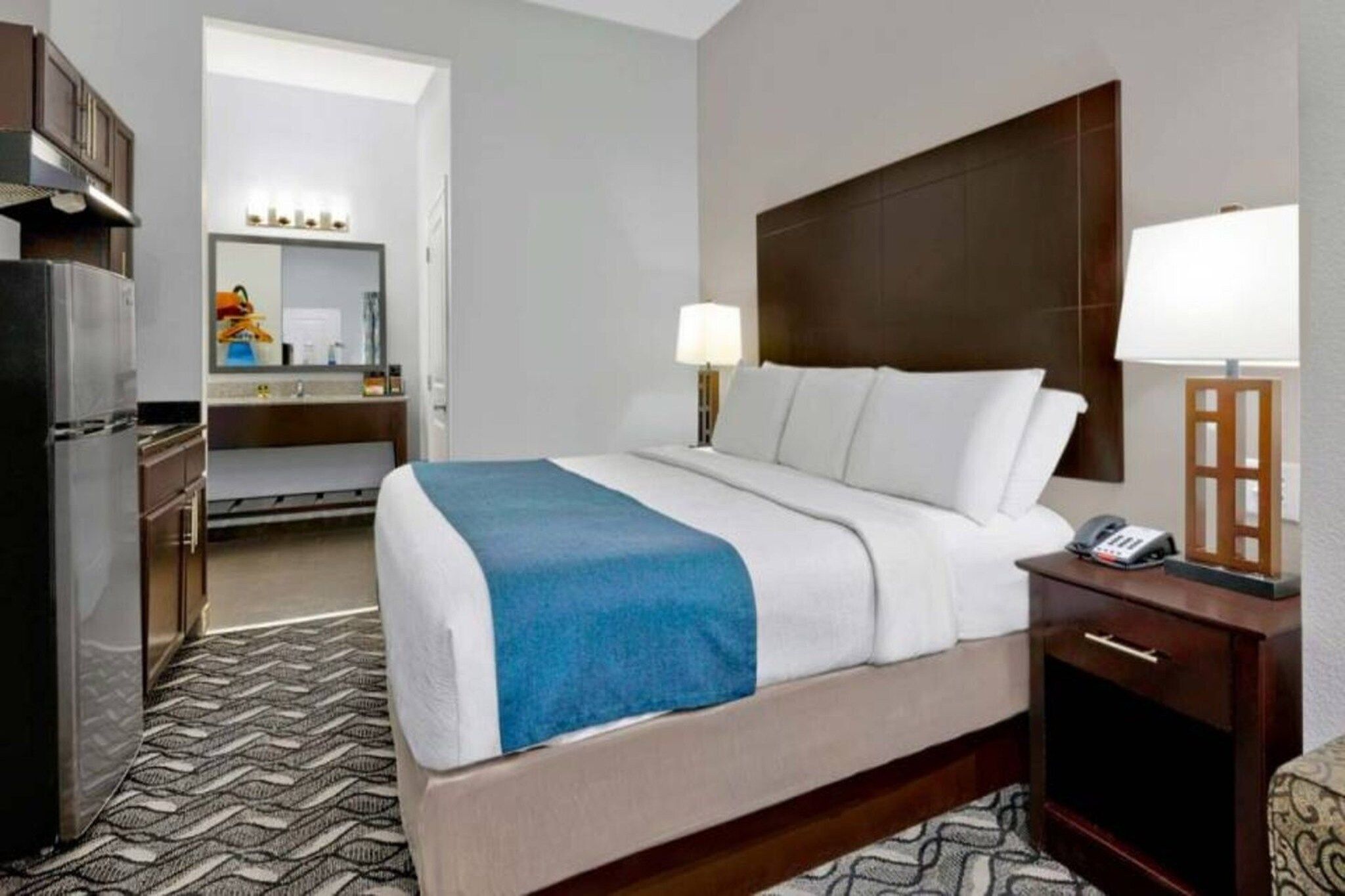 Ein Hotelzimmer mit Bett, Nachttisch, Lampe und einem Kühlschrank.