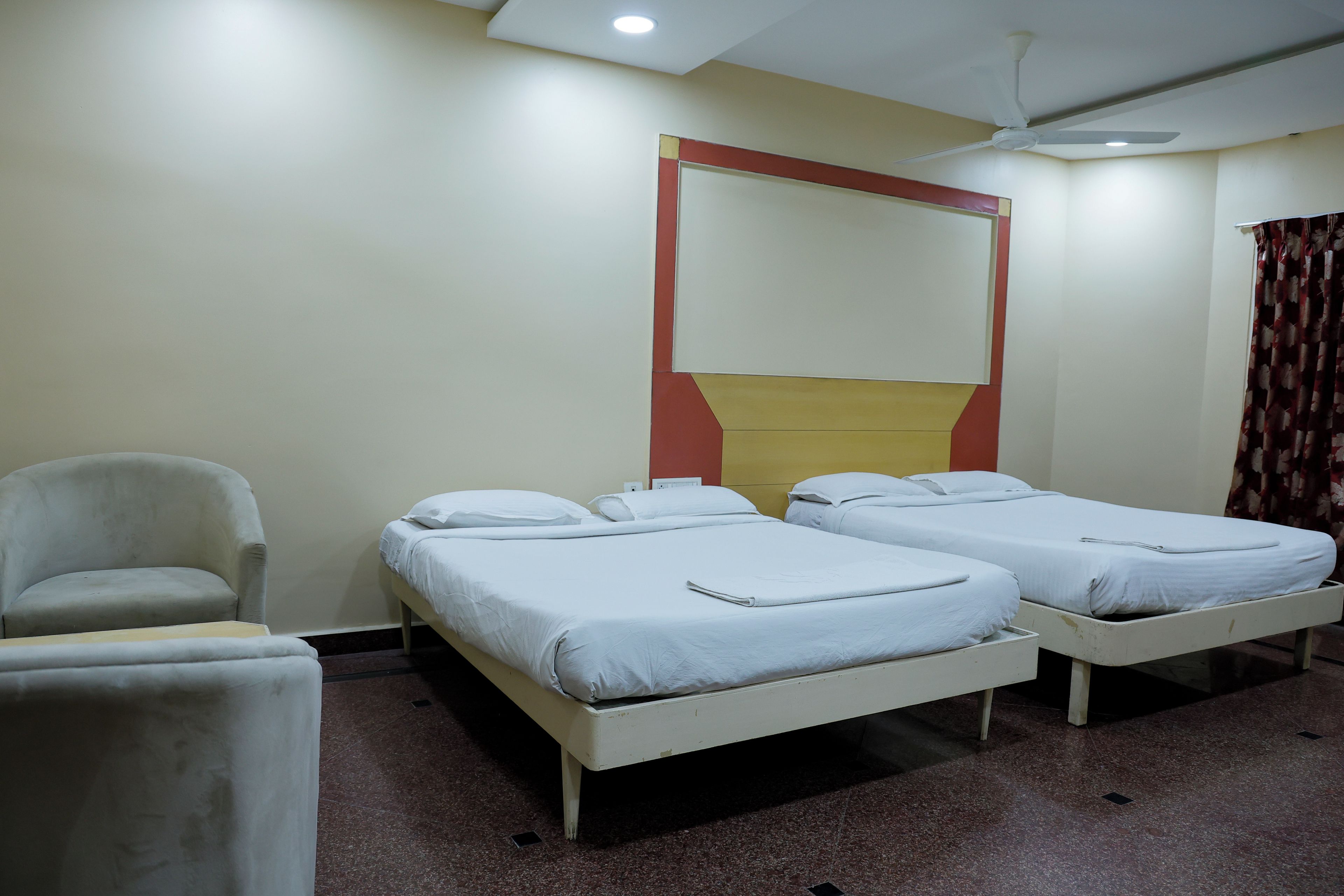 A hotel room with two single beds, a chair, and a ceiling fan.