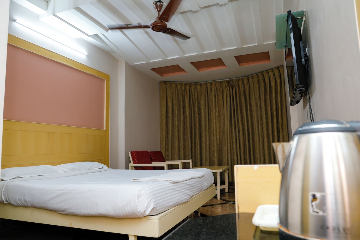 A hotel room with a bed, a chair, a desk, a coffee maker, and a ceiling fan.