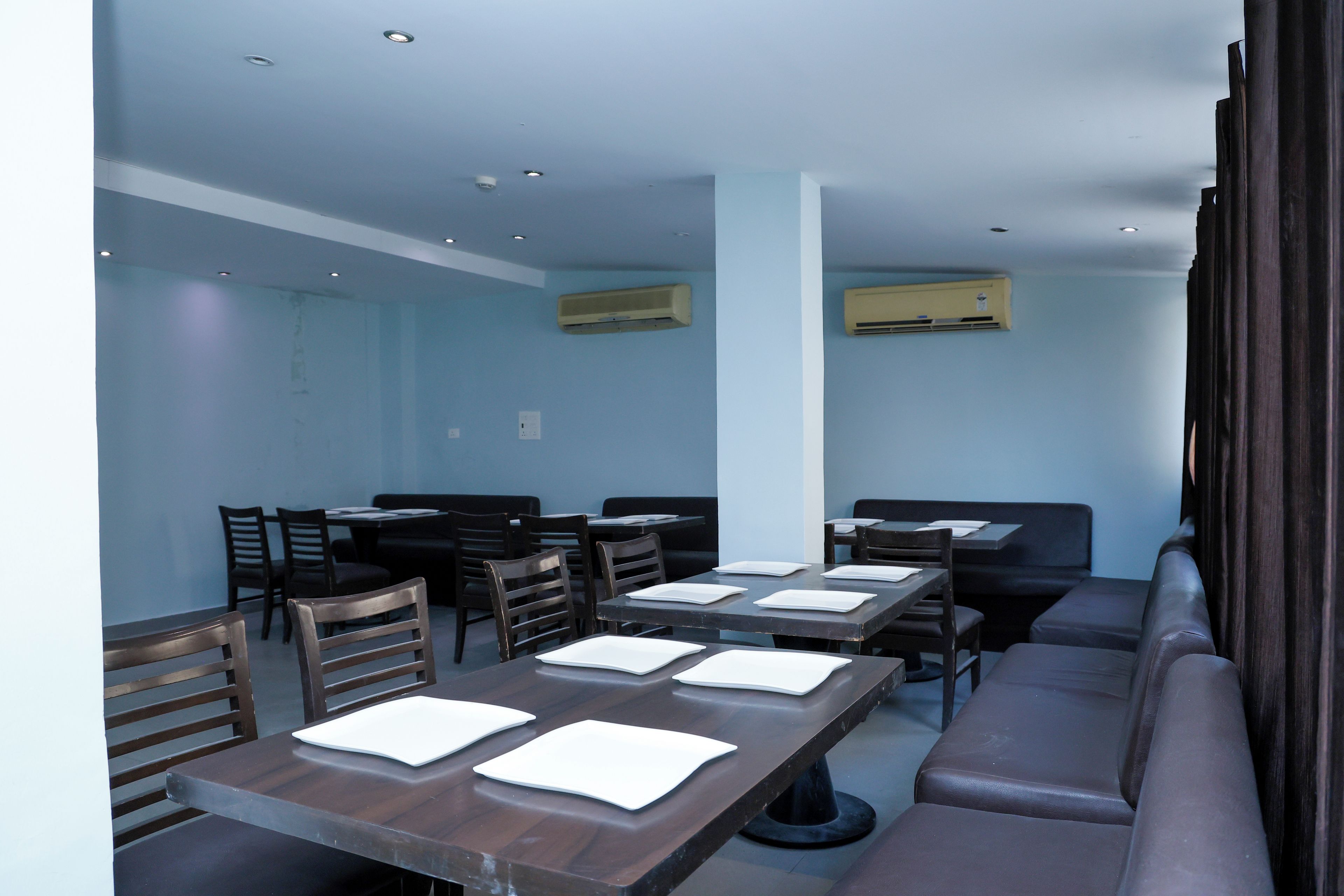 Un restaurant doté de nombreuses tables et chaises, de climatiseurs et d’un plafond haut.