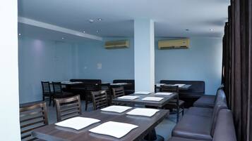 A restaurant with multiple tables and chairs, air conditioning units, and a high ceiling.