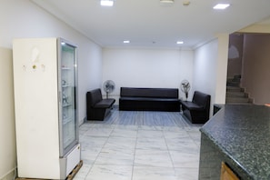 A reception area with a refrigerator, two black sofas, a marble-tiled floor, and a staircase in the background. - Hotel Raj Classic Inn (Secunderabad)