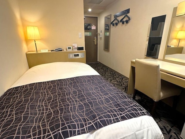 Habitación de hotel con cama, escritorio, silla, lámpara, espejo y puerta.