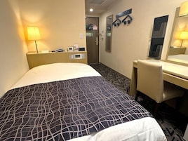 Habitación de hotel con cama, escritorio, silla, lámpara, espejo y puerta.