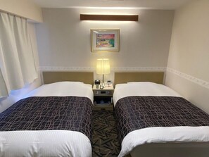 Habitación de hotel con dos camas, una mesita de noche con lámpara, un cuadro en la pared y una ventana con cortinas.