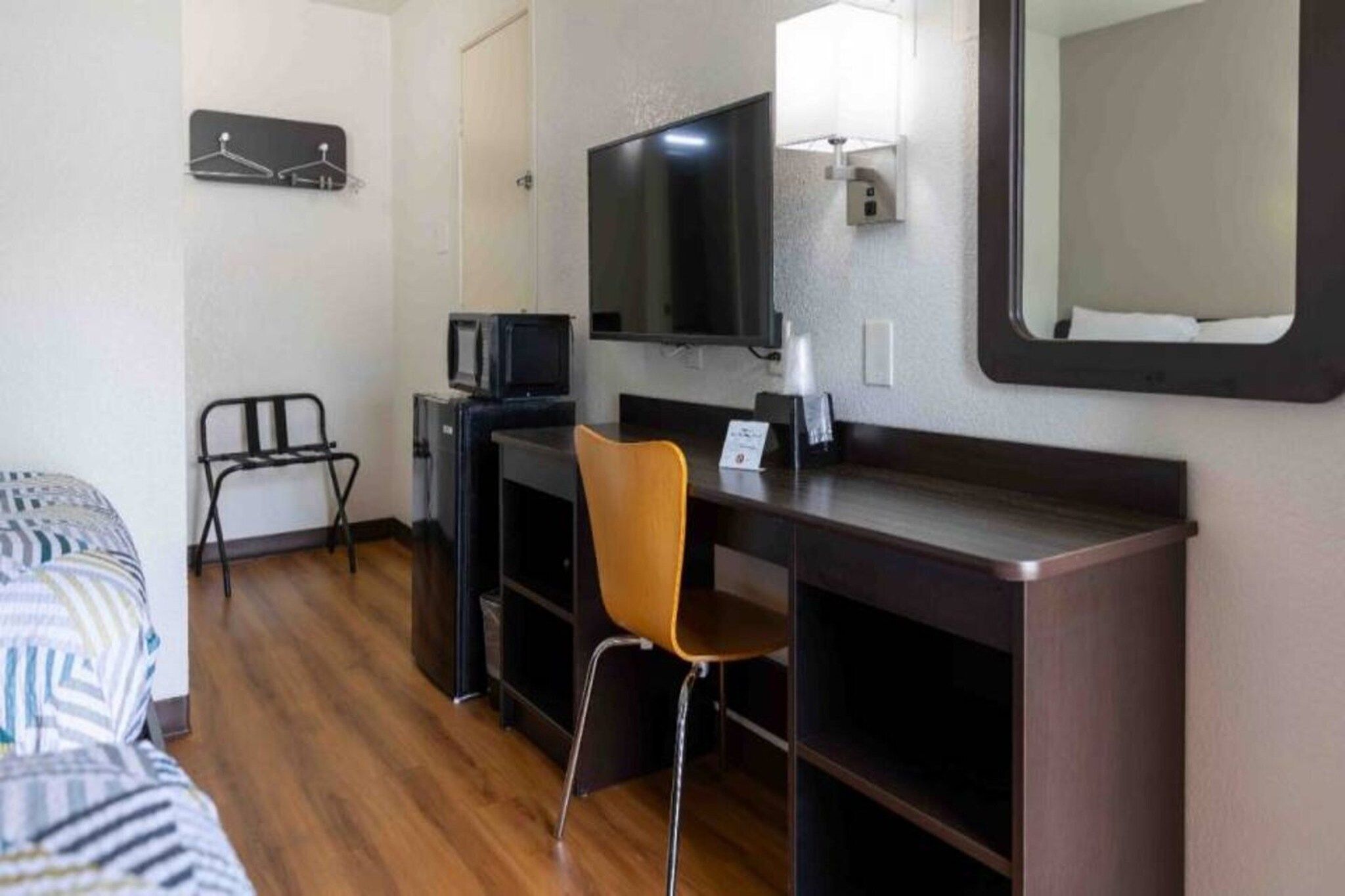 Quarto de hotel com cama, escrivaninha, cadeira, televisão e espelho.