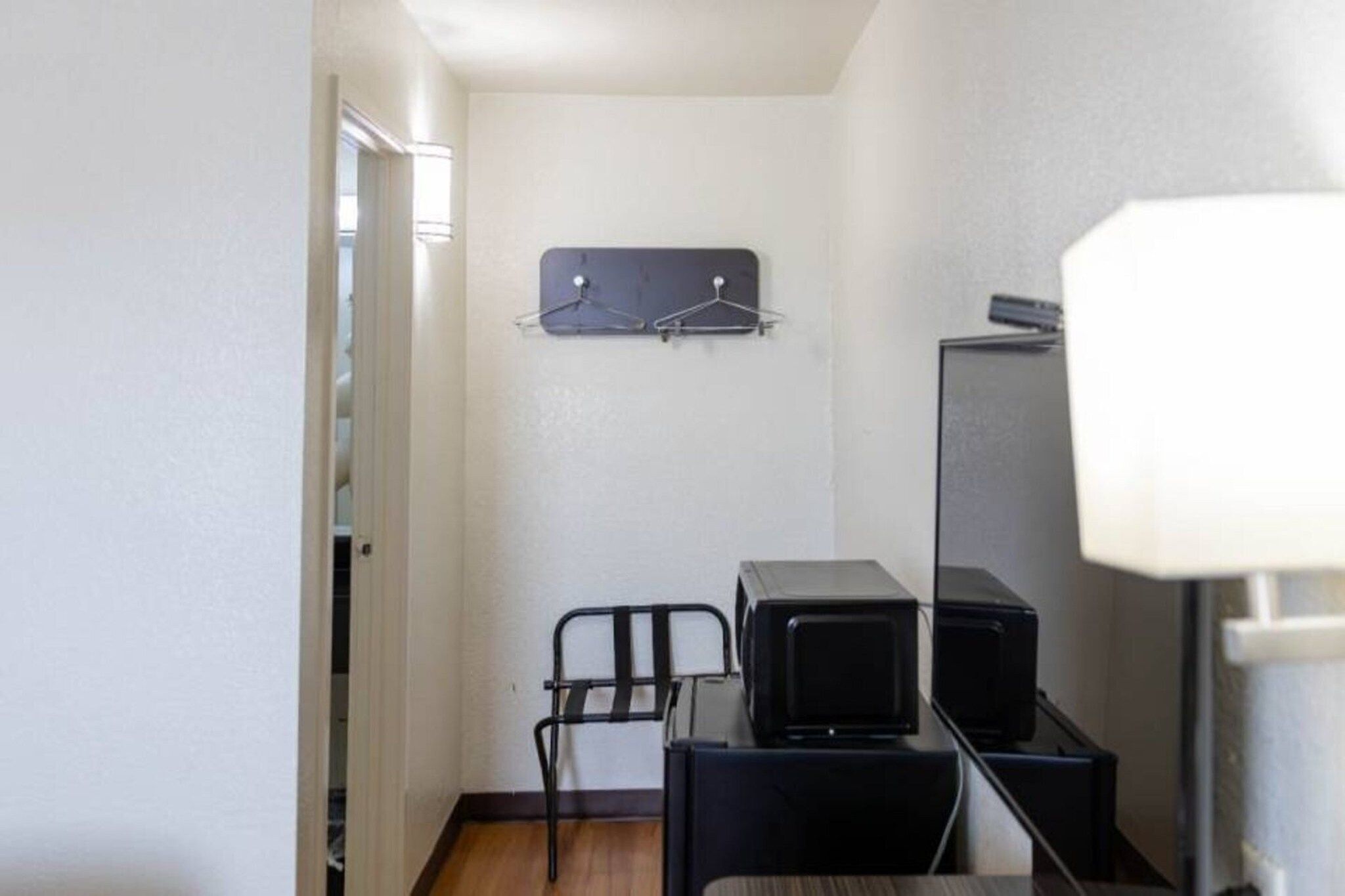 A narrow hallway with a coat rack, a chair, and a desk with a computer and a lamp.