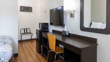 A hotel room with a bed, a desk with a chair, a television, and a mirror.