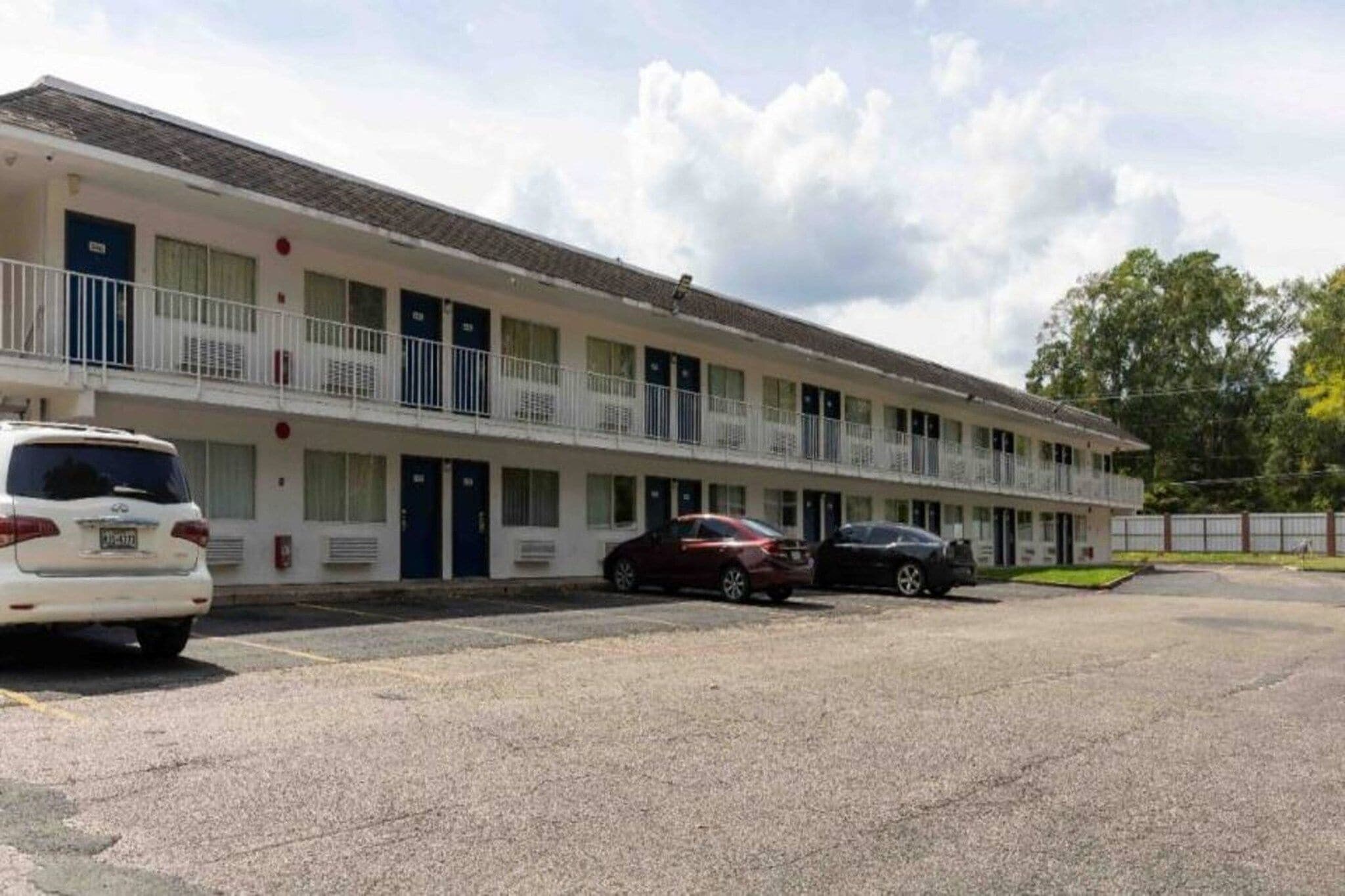 A motel with a row of rooms, a parking lot, and a building with a flat roof.