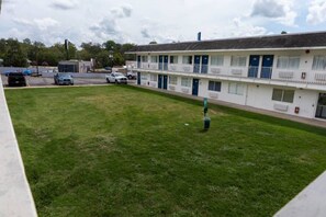 A motel with a grassy courtyard, a parking lot, and a building with multiple rooms.