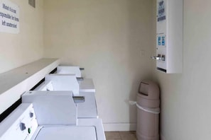 A laundry room with multiple washing machines and a trash bin.