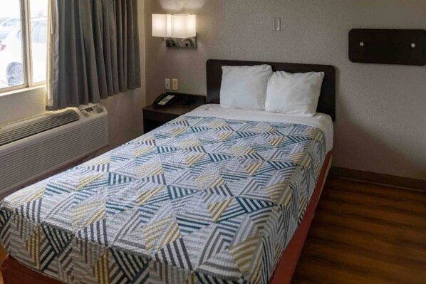 Une chambre d’hôtel avec un lit, une table de chevet avec une lampe, un téléphone et une fenêtre avec des rideaux.