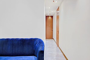 Un pasillo con un sofá azul, una puerta de madera y un piso de mármol.