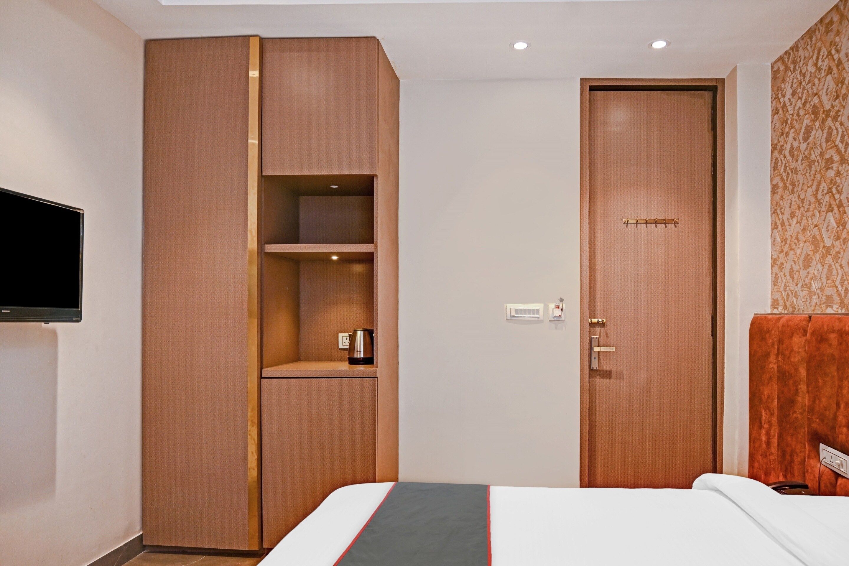 A hotel room with a bed, a wardrobe, a television, and a door.