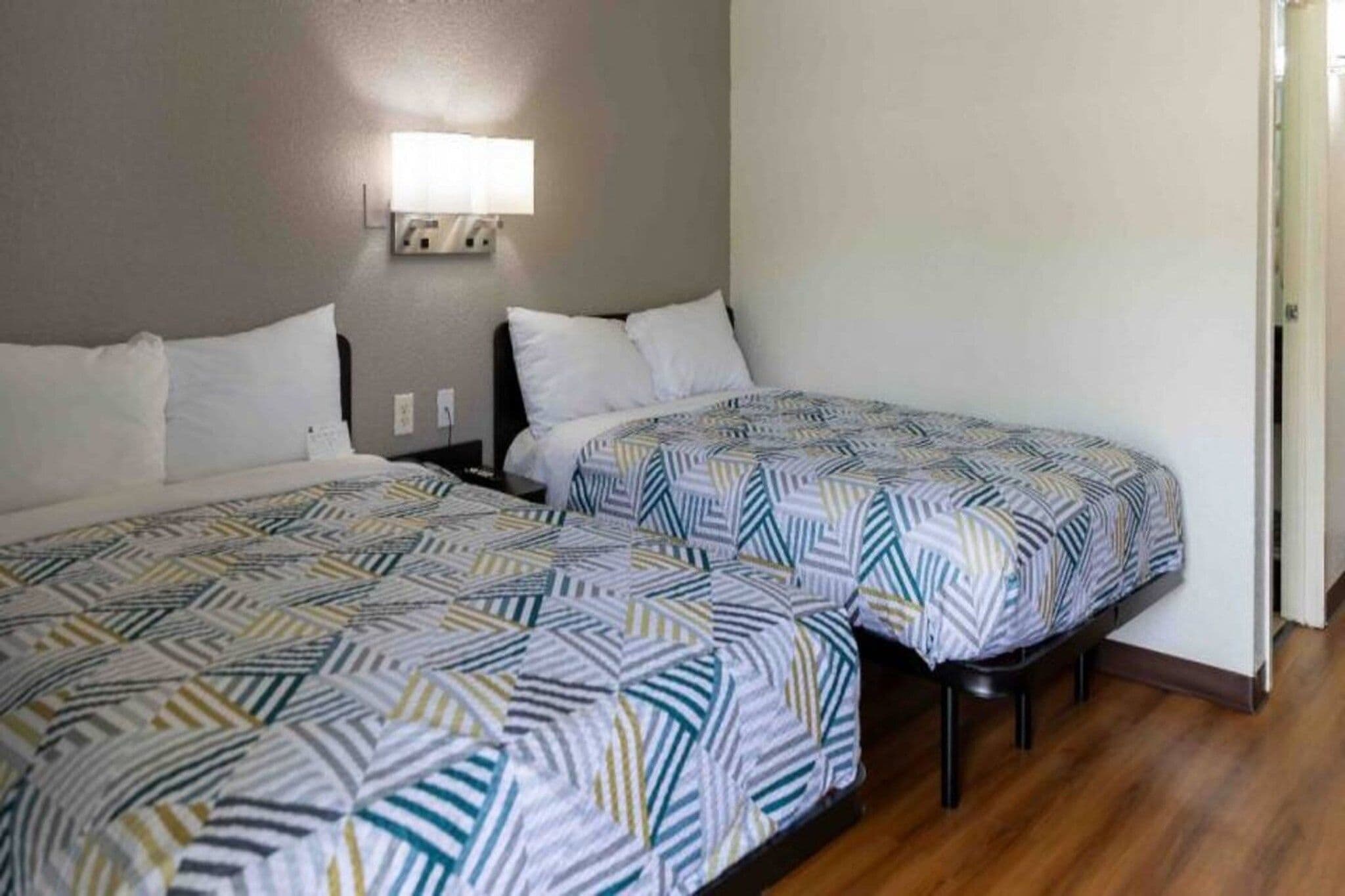 A hotel room with two beds, a nightstand, and a wall-mounted light.