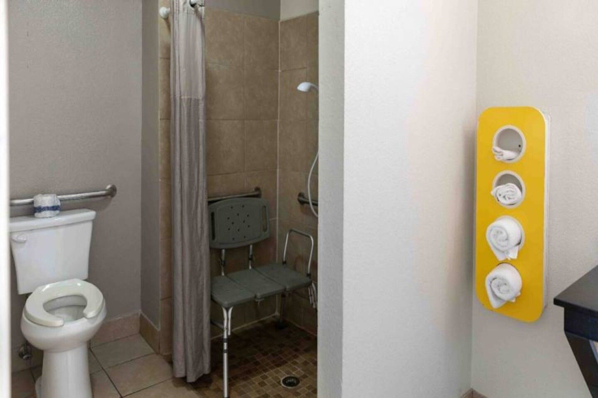 Casa de banho com sanita, chuveiro e um porta-toalhas amarelo.