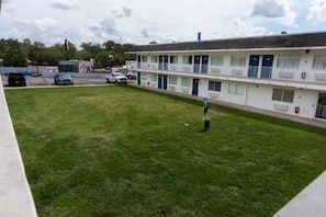 A motel with a grassy courtyard, a parking lot, and a building with multiple rooms.