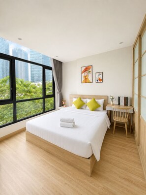 A hotel room with a large bed, a desk, and a view of city buildings. - 8 Nguyen Van Ngoc (BA DINH)