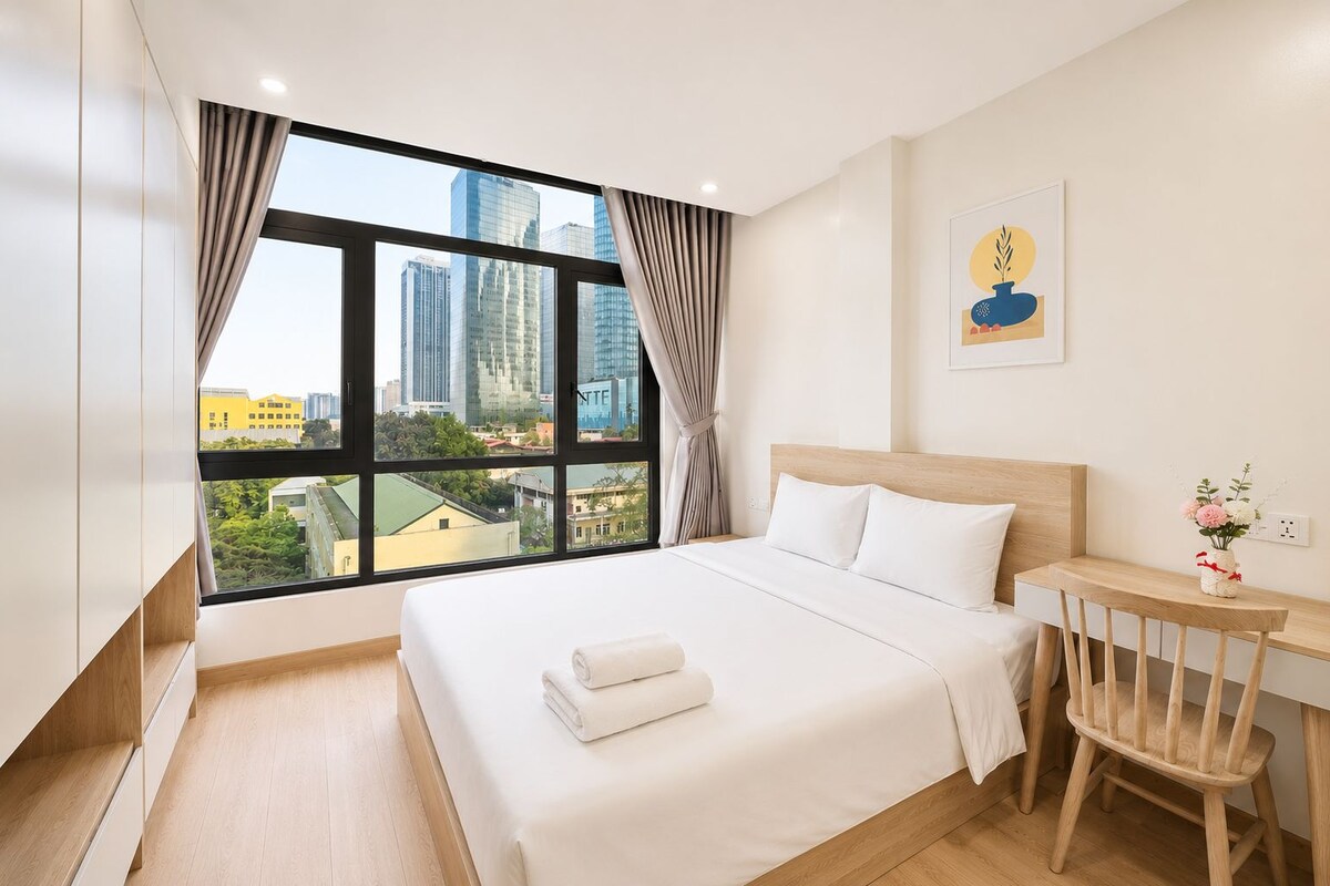 A hotel room with a large window, a bed with white linens, a wooden nightstand, and a chair.