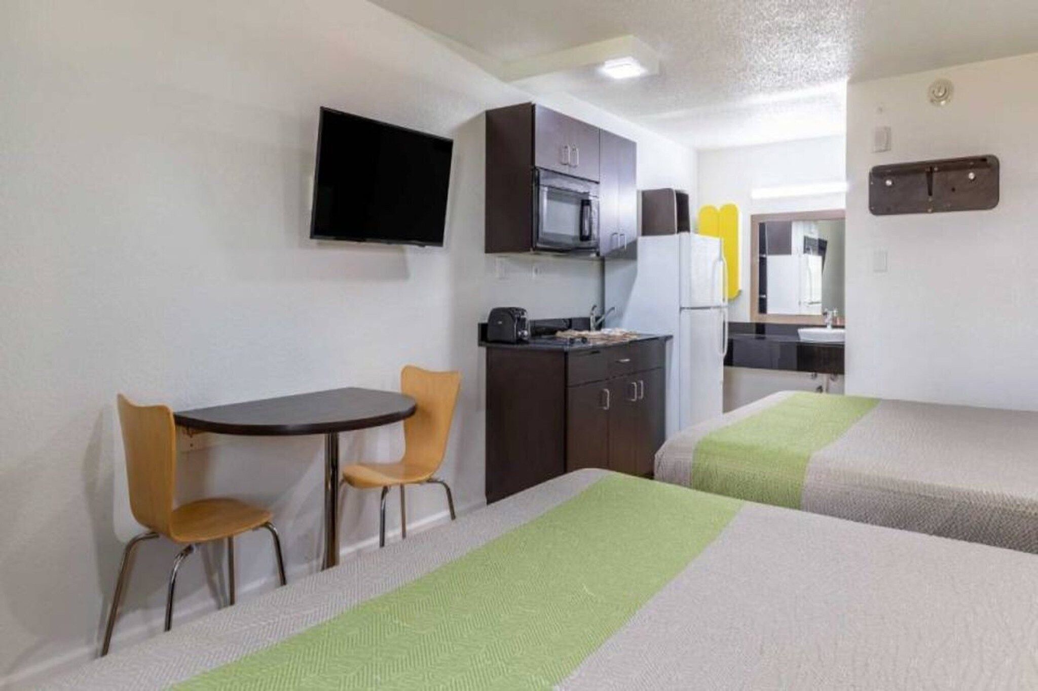 Une chambre d’hôtel compacte comprenant un coin cuisine, une télévision, un coin repas avec deux chaises et deux lits.