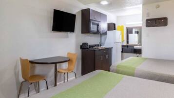 Une chambre d’hôtel compacte comprenant un coin cuisine, une télévision, un coin repas avec deux chaises et deux lits.