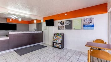 Un espace d’accueil comprenant un comptoir, un téléviseur fixé au mur, un présentoir à magazines et une table avec des chaises.