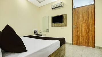 A hotel room with a bed, a flat-screen TV mounted on the wall, an air conditioning unit, and a wooden door.