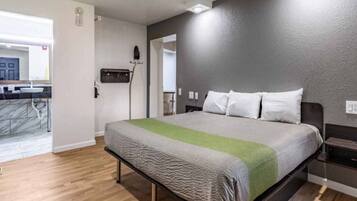A hotel room with a bed, a nightstand, a wall-mounted heater, and a view of the bathroom.