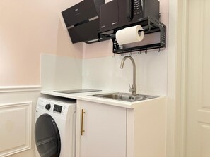 Una cocina compacta con lavadora integrada, un lavamanos y un microondas.