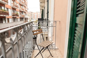Un balcón estrecho con barandilla de metal, un banco de madera y vistas a edificios cercanos.