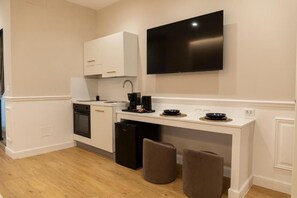A compact kitchen with white cabinetry, a black refrigerator, a coffee maker, and a flat-screen TV mounted on the wall. - Mas Collection - Dimora Zonno 1st Floor (Bari)