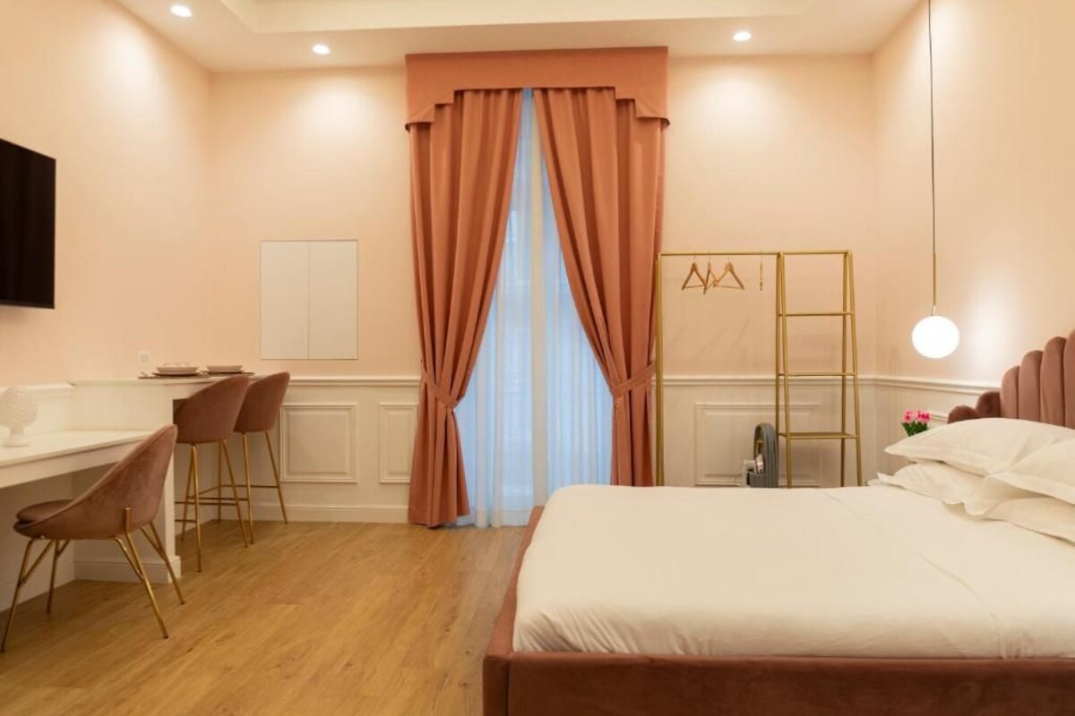 A hotel room with a bed, a desk with chairs, a wardrobe, and a hanging light fixture.