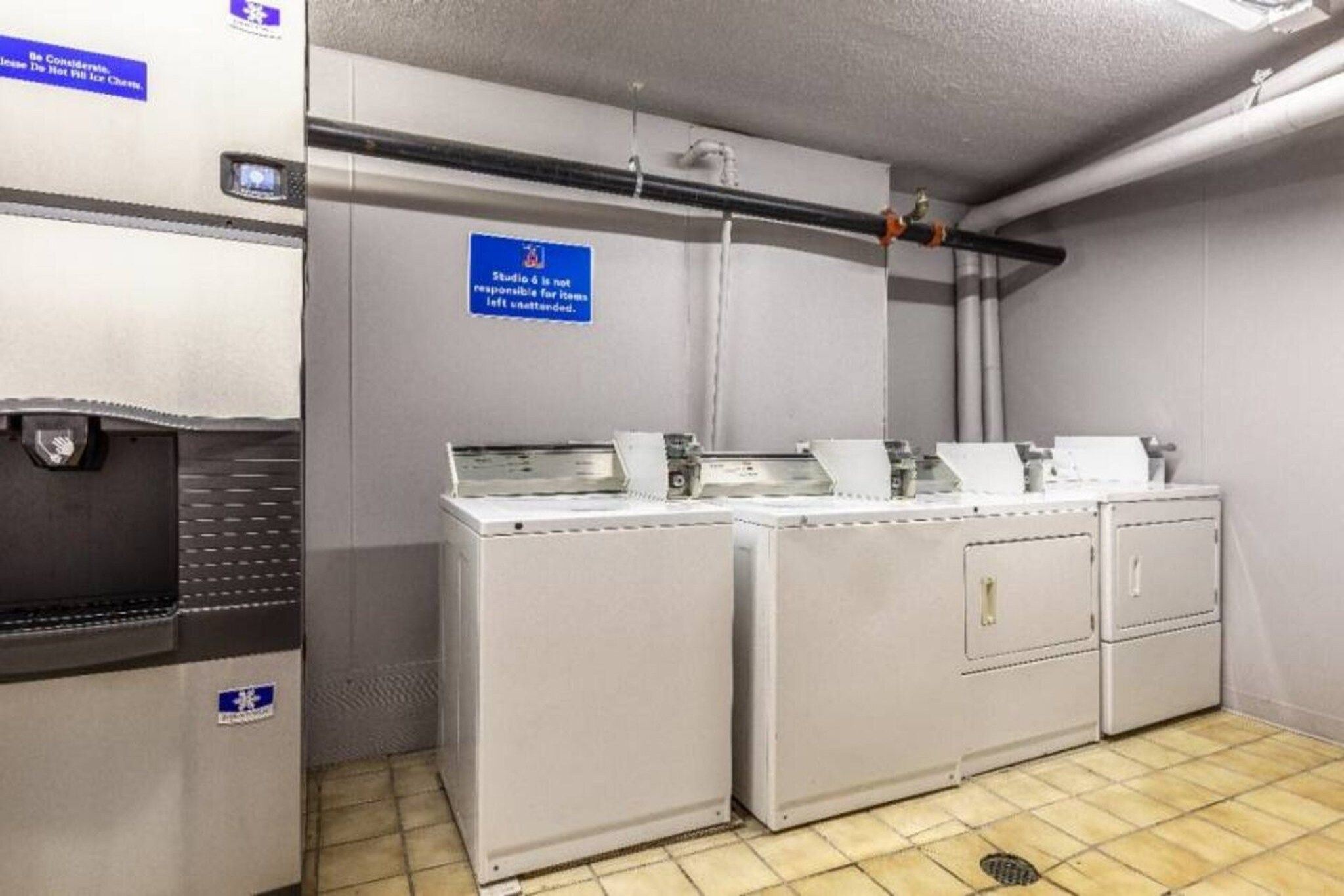 Une buanderie équipée de machines à laver et de séchoirs industriels, un panneau indiquant que cet espace n’est pas accessible au public, et une main courante fixée au mur.