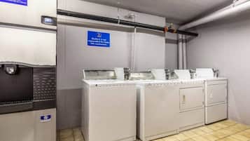 Une buanderie équipée de machines à laver et de séchoirs industriels, un panneau indiquant que cet espace n’est pas accessible au public, et une main courante fixée au mur.