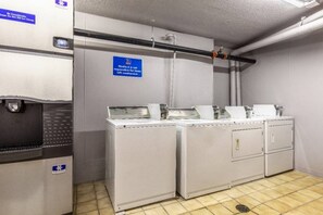 Une buanderie équipée de machines à laver et de séchoirs industriels, un panneau indiquant que cet espace n’est pas accessible au public, et une main courante fixée au mur.