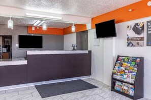 Un espace d’accueil comprenant un comptoir, un téléviseur à écran plat, un présentoir à magazines et une porte donnant sur une autre pièce.