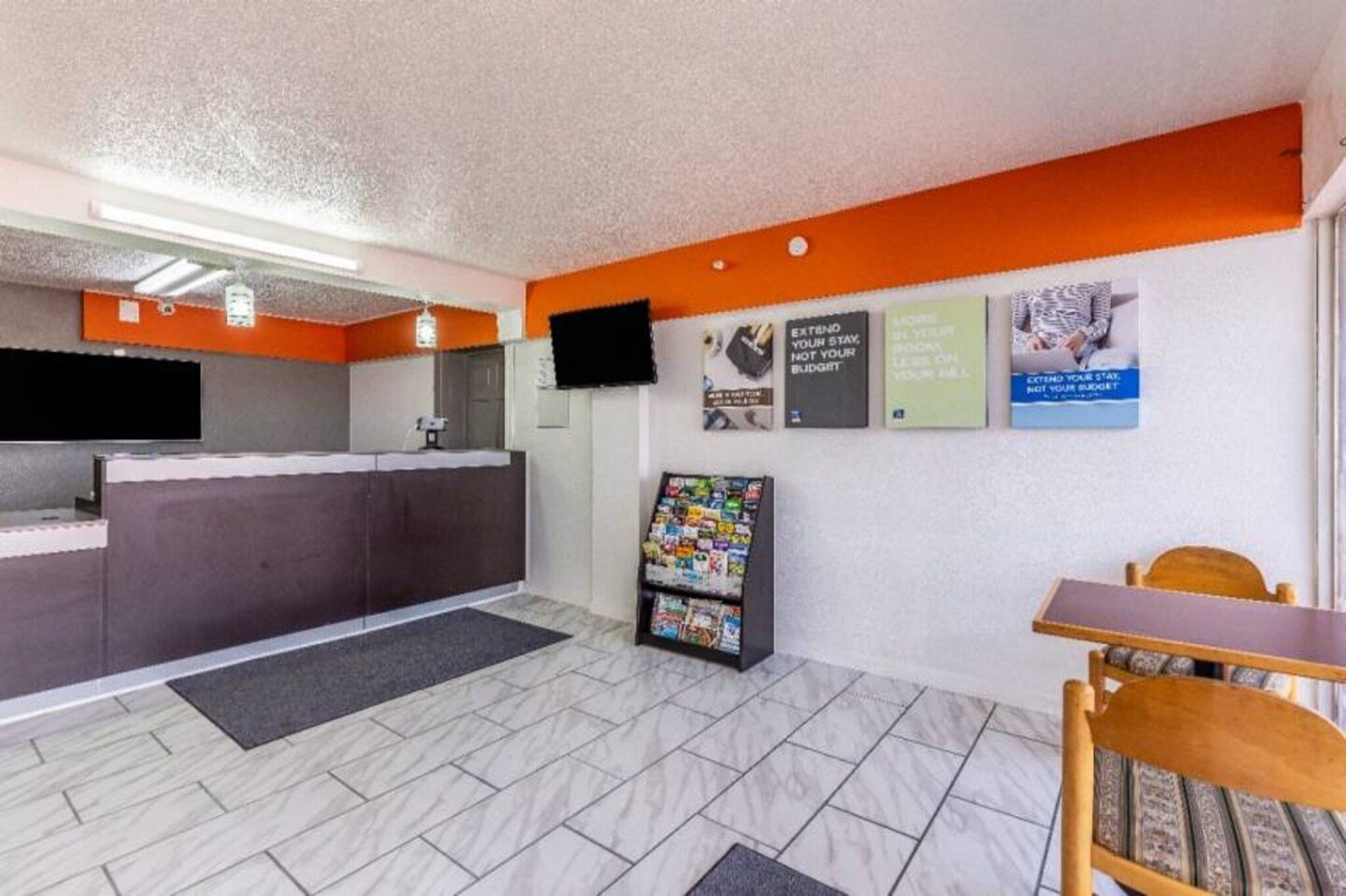 A reception area with a counter, a television mounted on the wall, a magazine rack, and a table with chairs.