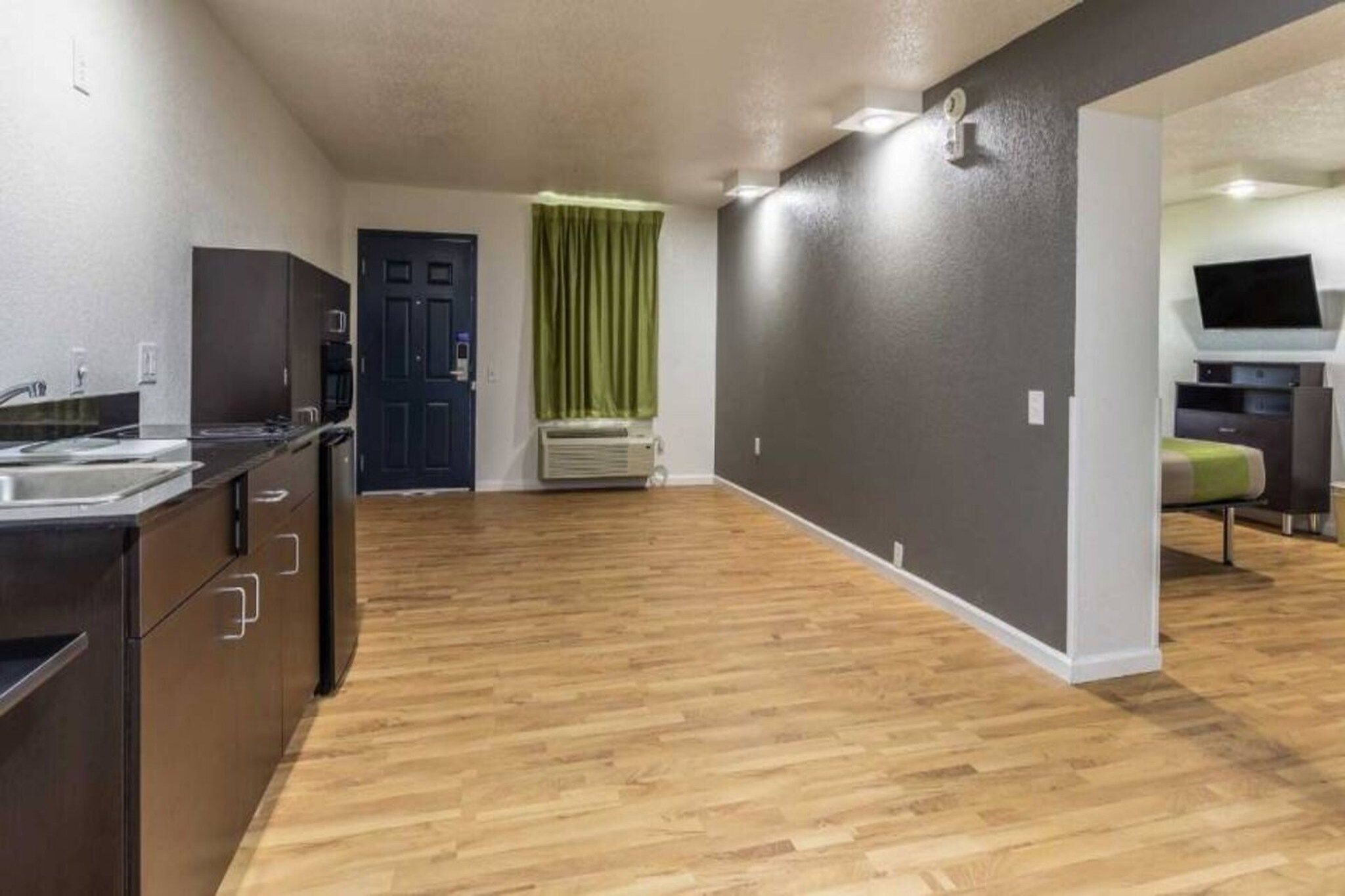 A modern kitchen with a built-in oven, a microwave, and a sink. There is a door with a window and a green curtain.