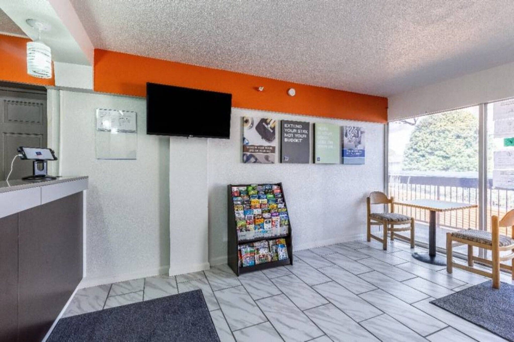 Un espace d’accueil comprenant un comptoir, un téléviseur fixé au mur, un présentoir à magazines et un coin salon avec des chaises.