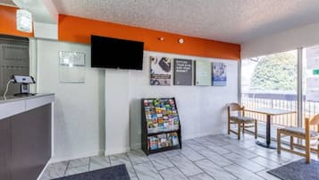 Un espace d’accueil comprenant un comptoir, un téléviseur fixé au mur, un présentoir à magazines et un coin salon avec des chaises.